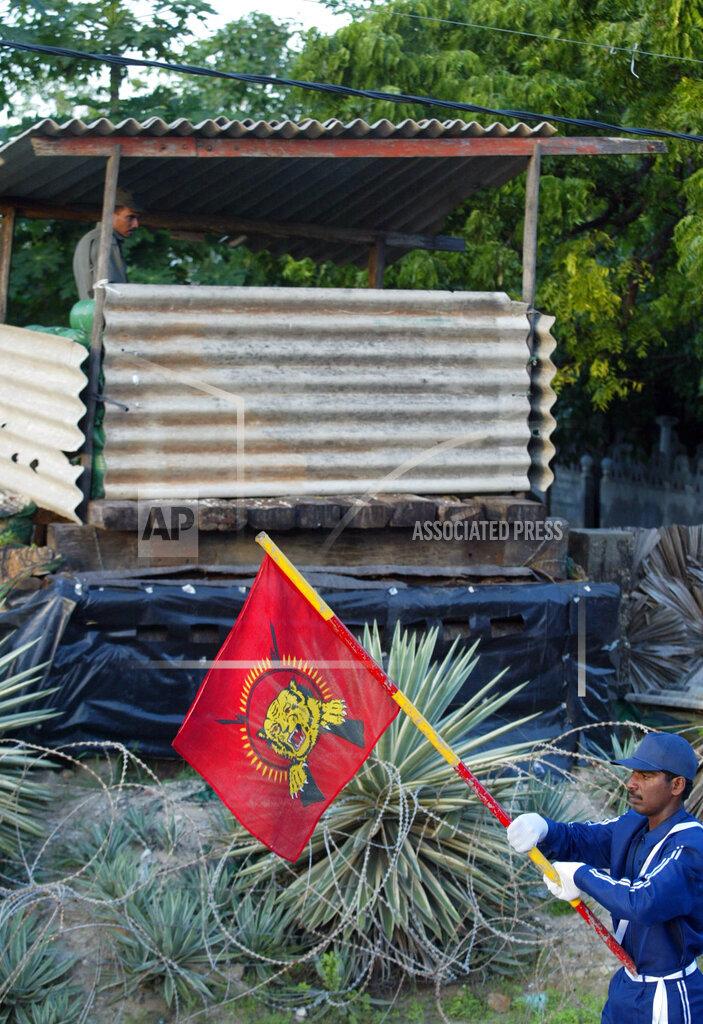 A Tamil youth, a member of a rebel volunteer force marches with a flag of Tamil Eelam past a Sri Lankan government soldier, during a ceremony to celebrate the 51st birthday of Tamil rebel leader.jpg
