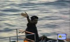 A male Sea Black Tiger riding a Kifir class boat waving his hand towards his friends one lat time who are standing in seashore.jpg